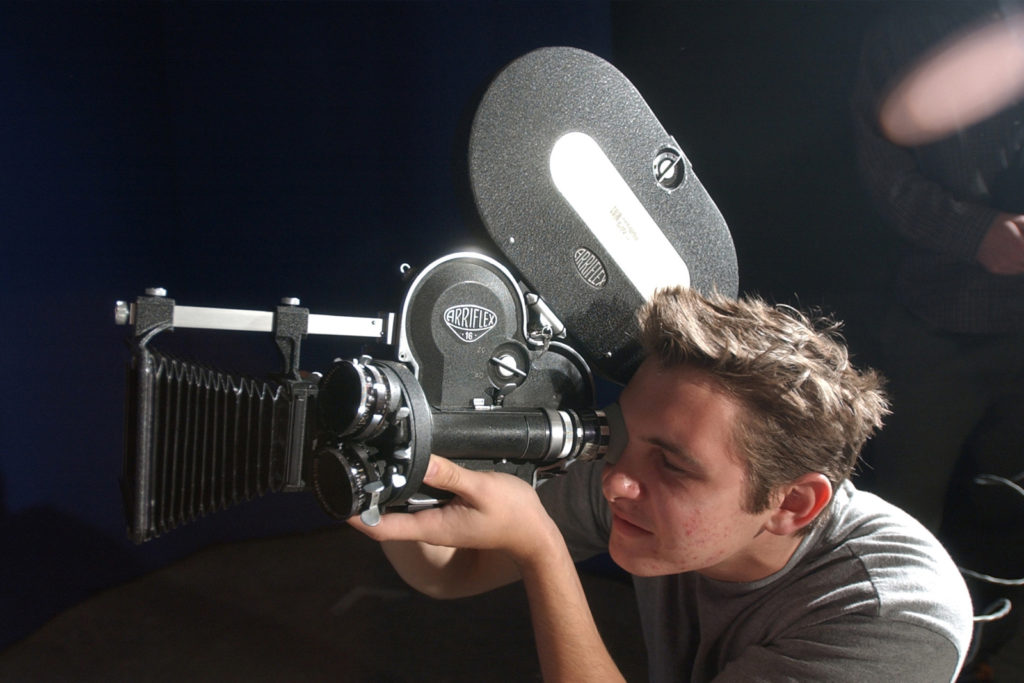 A student peering into a film camera.