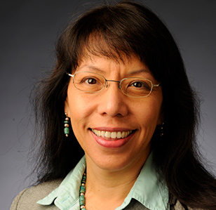person with long dark hair, mint colored shirt, earrings and glasses poses for a headshot