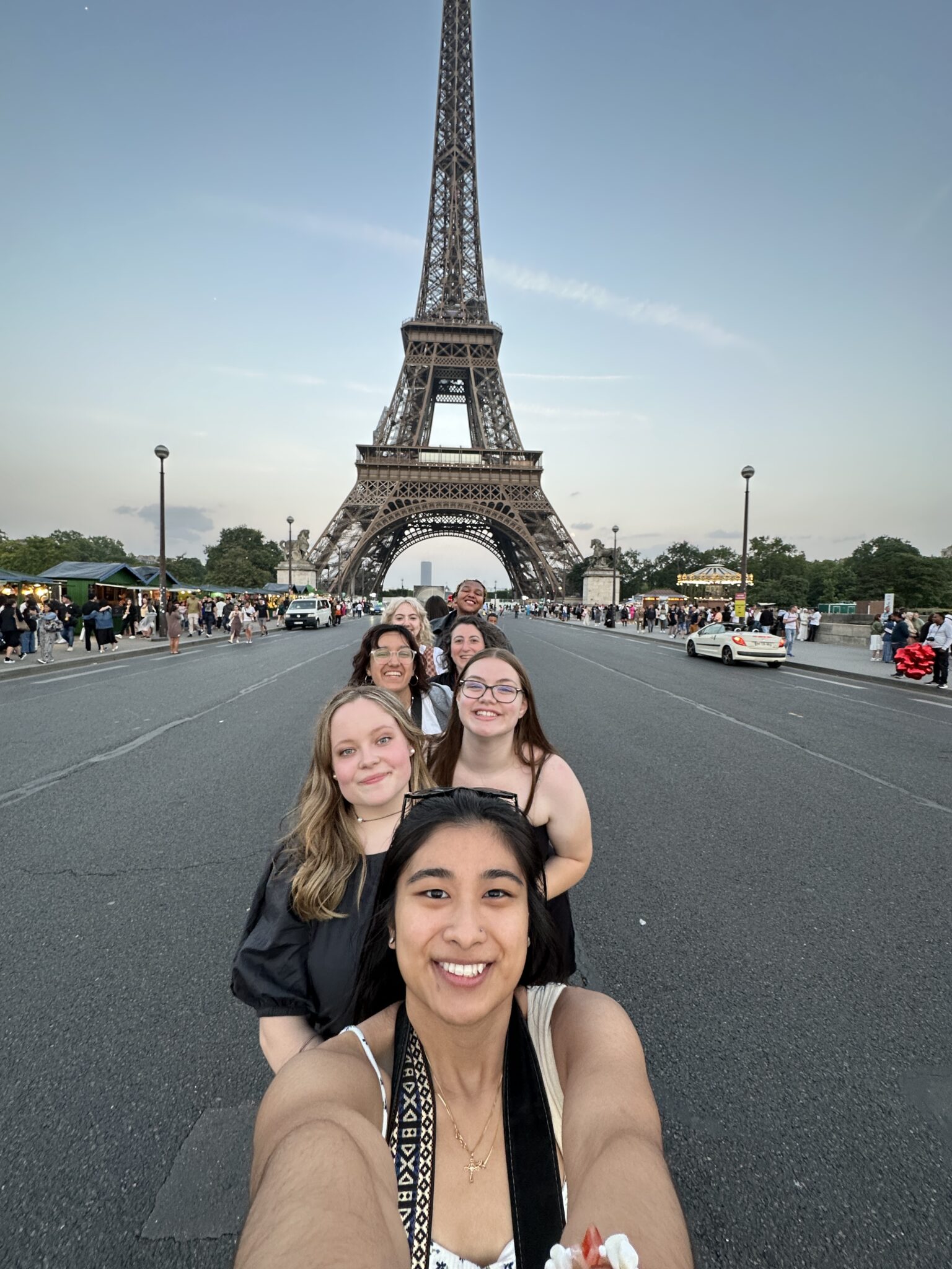 A group of students and their professor take a selfie in front of the Eiffel Tower in Paris France.