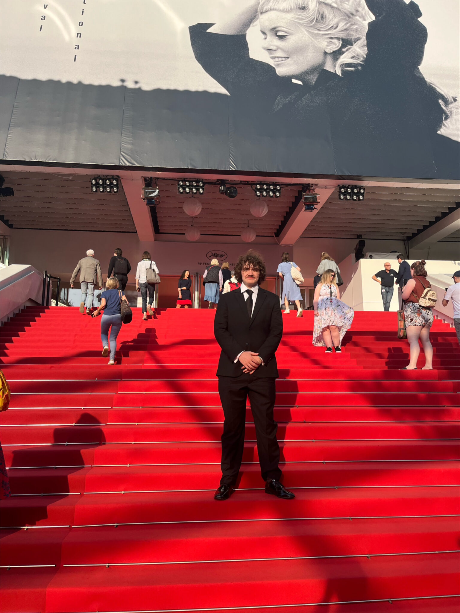 A man in a black suit stands on the red carpeted steps at the Cannes Film Festival