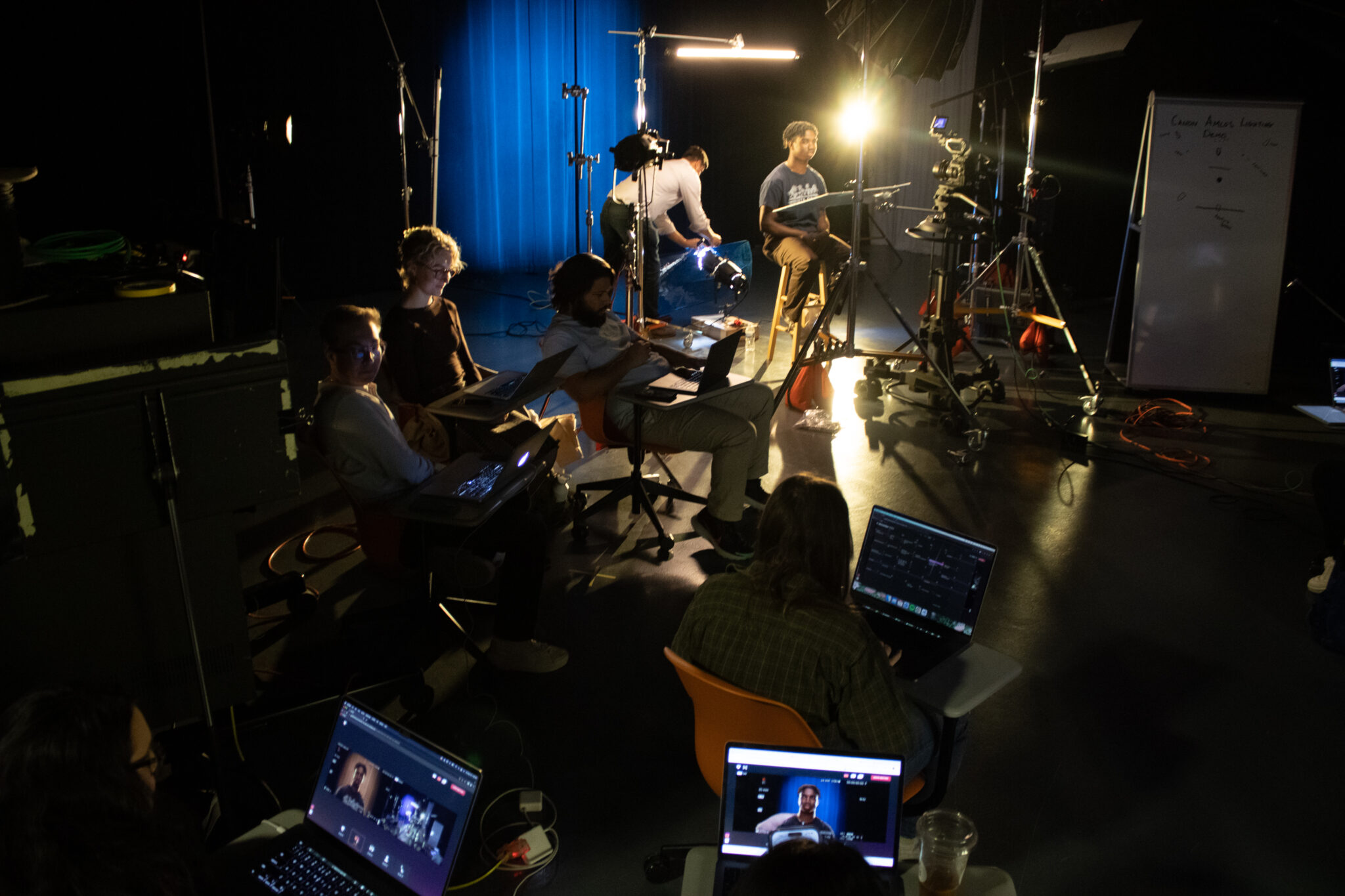 students look at their laptops in a dark photo studio