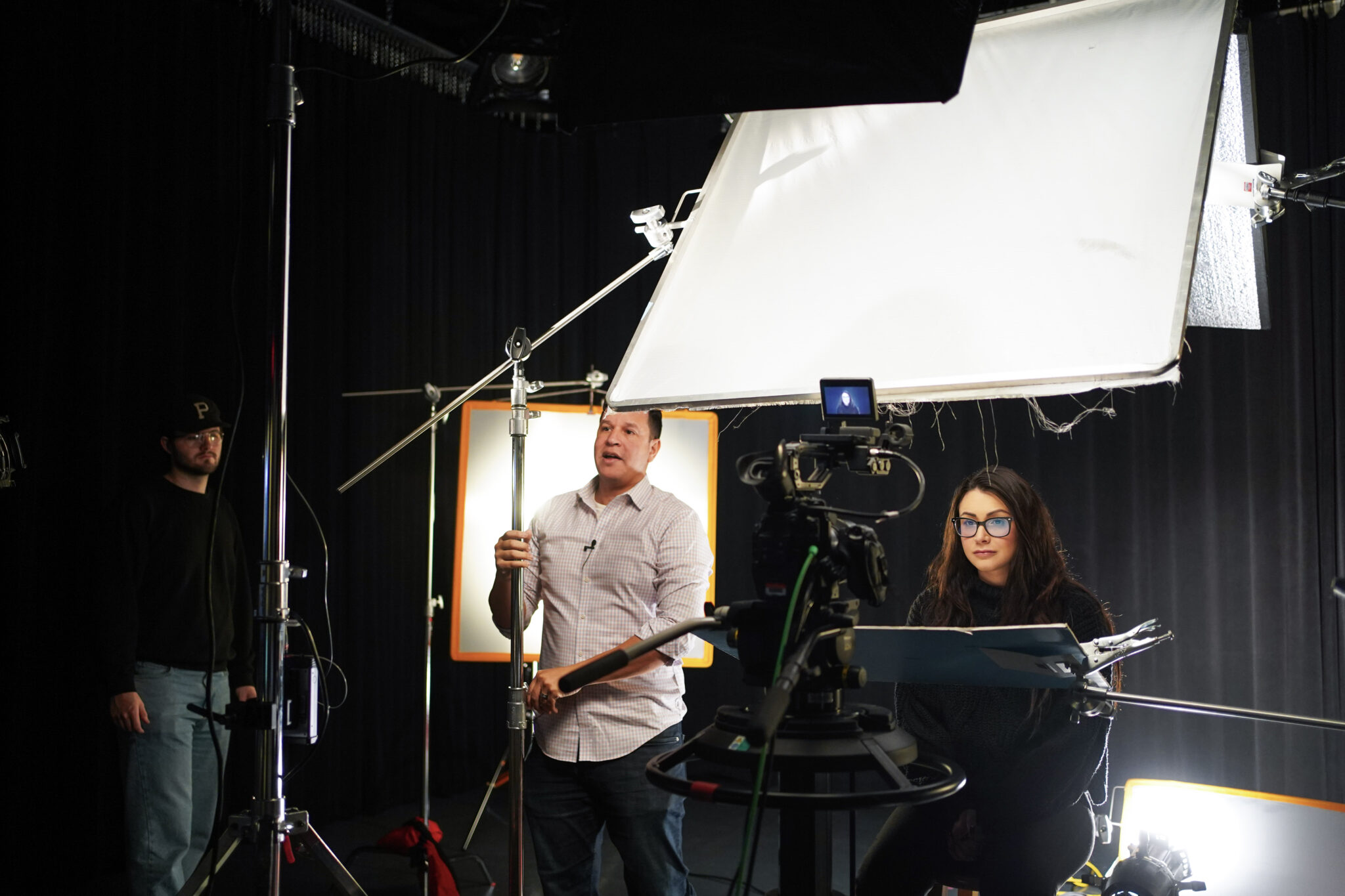 A professor demonstrates lighting setups in a photo studio with a student.