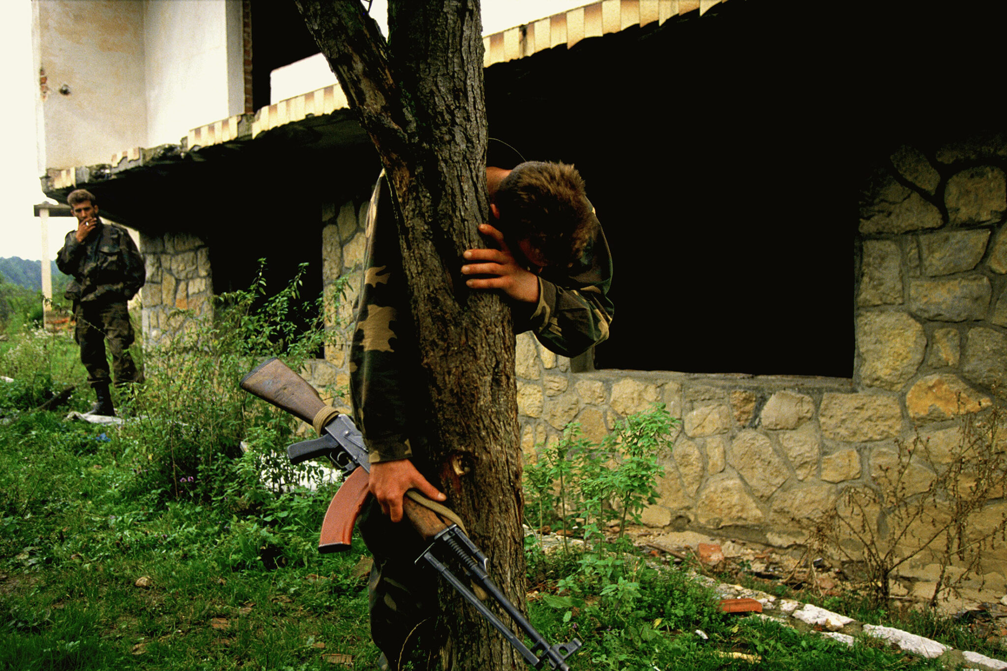 a soldier cries while holding onto a tree trunk