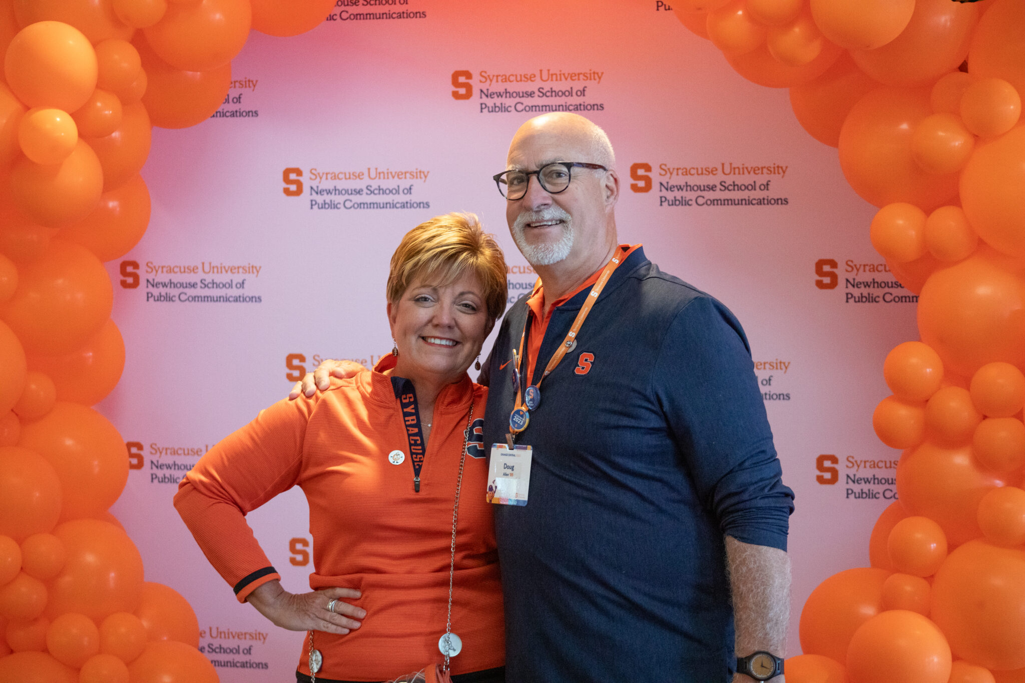 two people pose together in front of orange balloons and smile