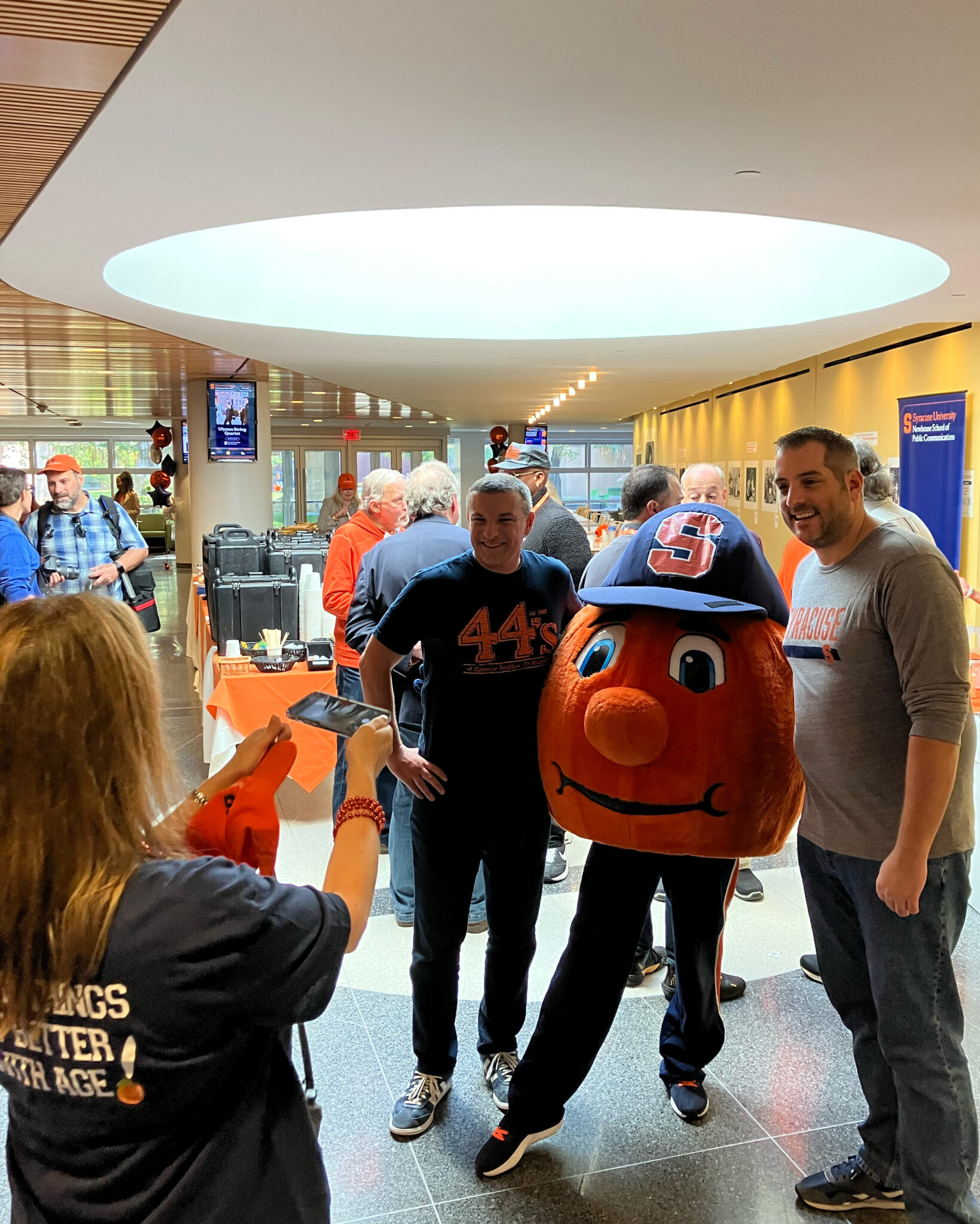 a woman takes a photo of two men posing with a mascot