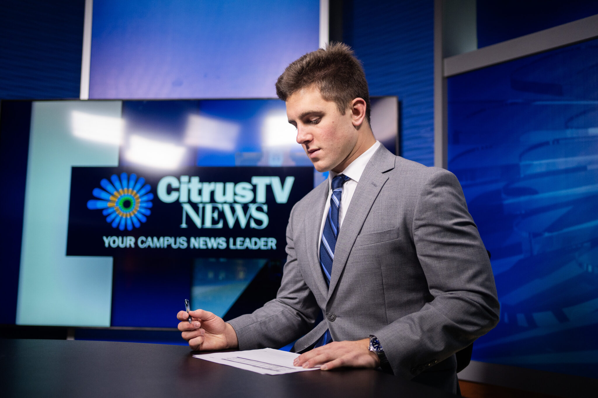 A man sits behind the anchor desk in a television studio