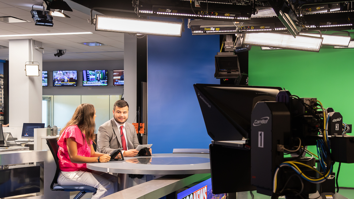 two students sit at anchor desk in Newhouse production studio