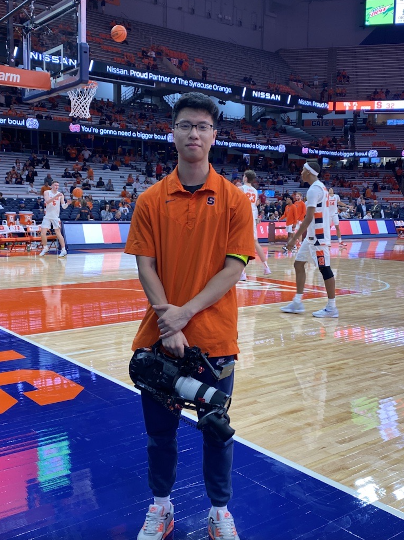 A student standing at a basketball game holding a camera 