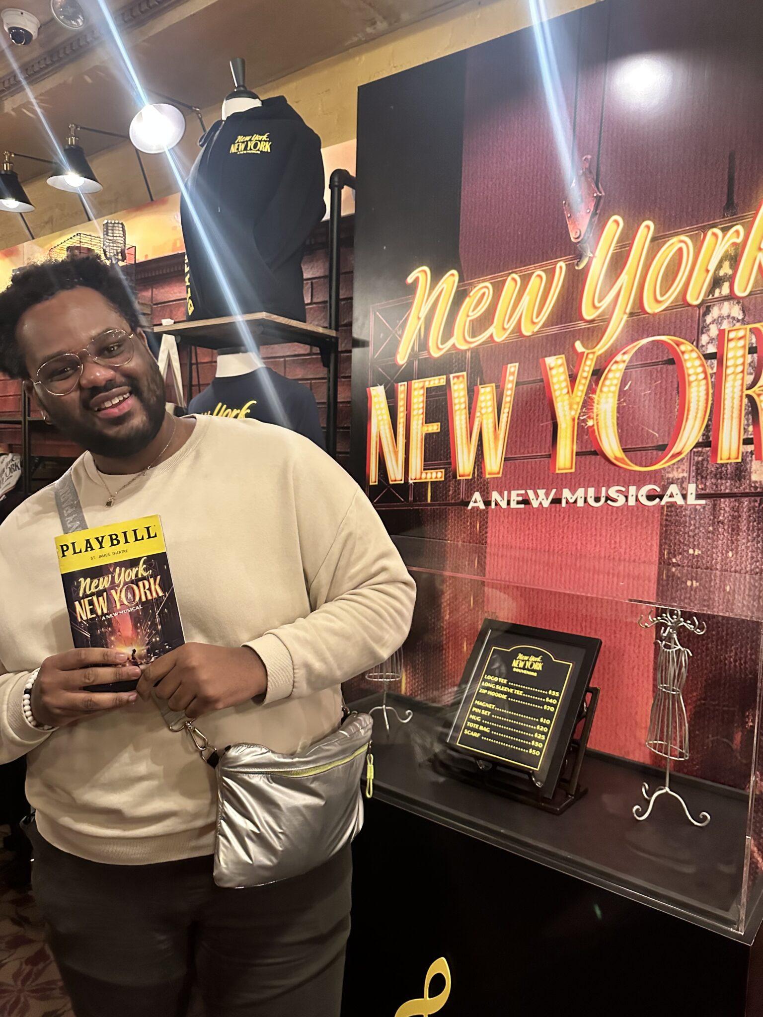 Rayshaun Sandlin holds a Playbill while posing next to a poster for a musical