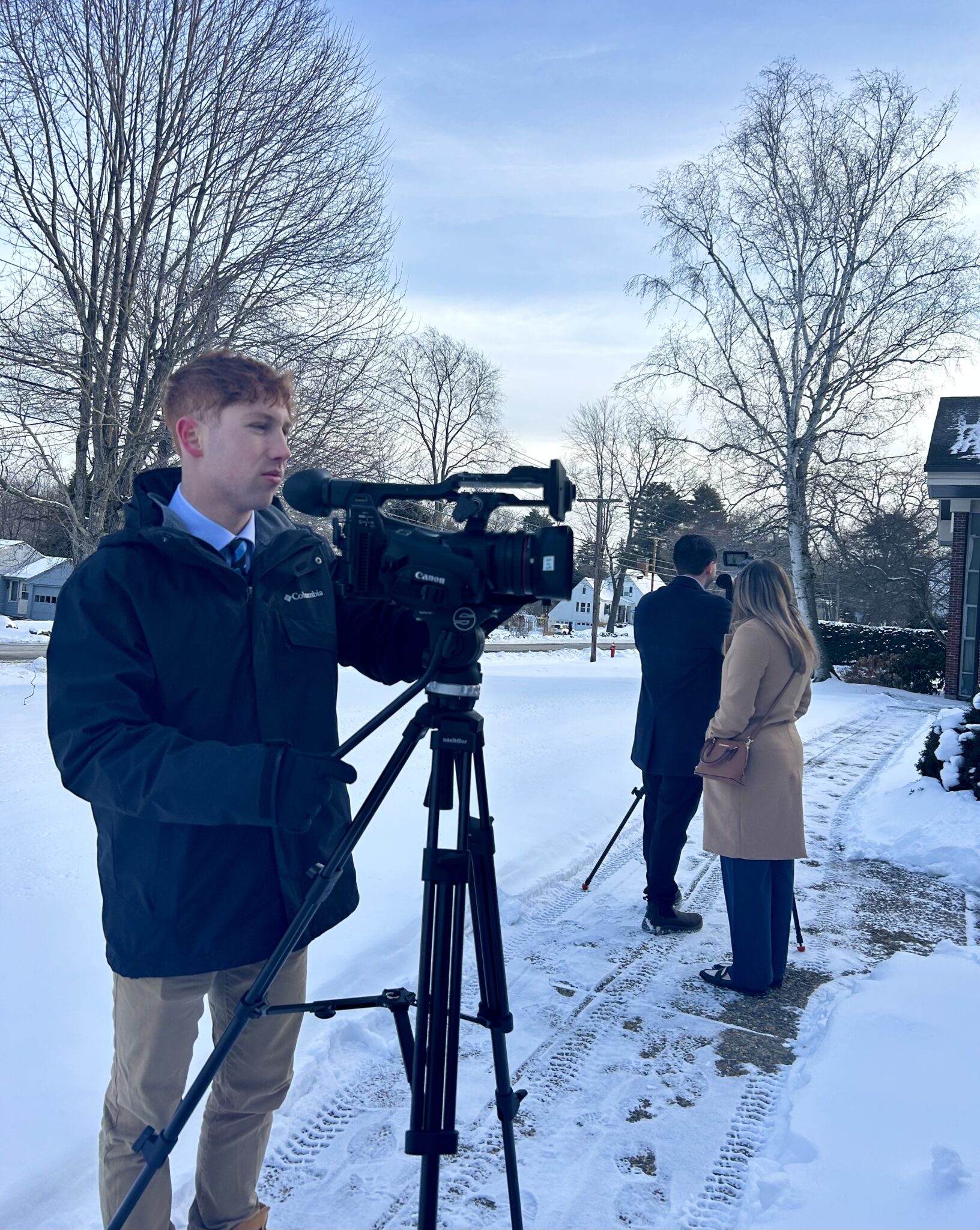 three people film with news cameras while standing outside in the snow