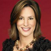 a person with light brown hair wears a necklace and black shirt and smiles for the camera in a professional headshot.