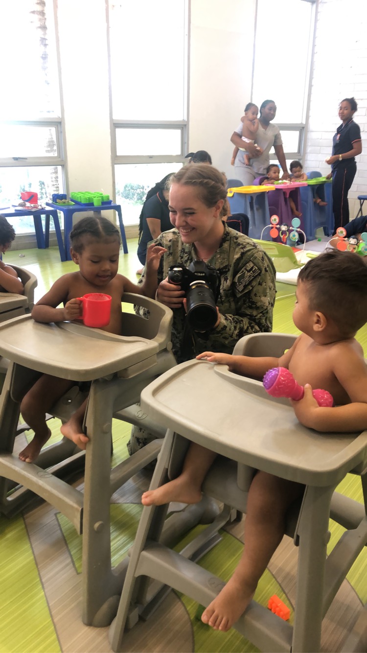 a person smiles while holding a camera and interacting with children