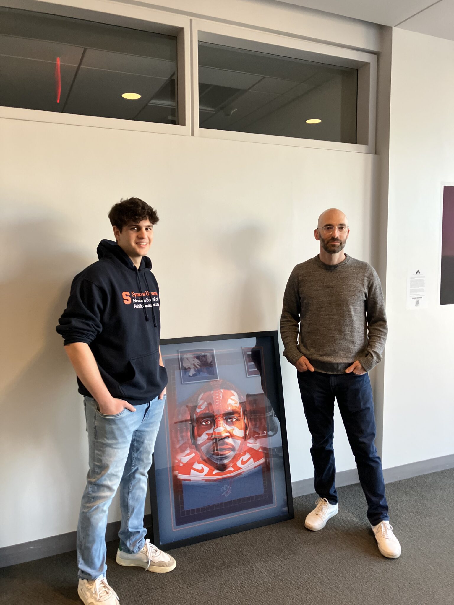 Two people stand together with a framed photograph between them
