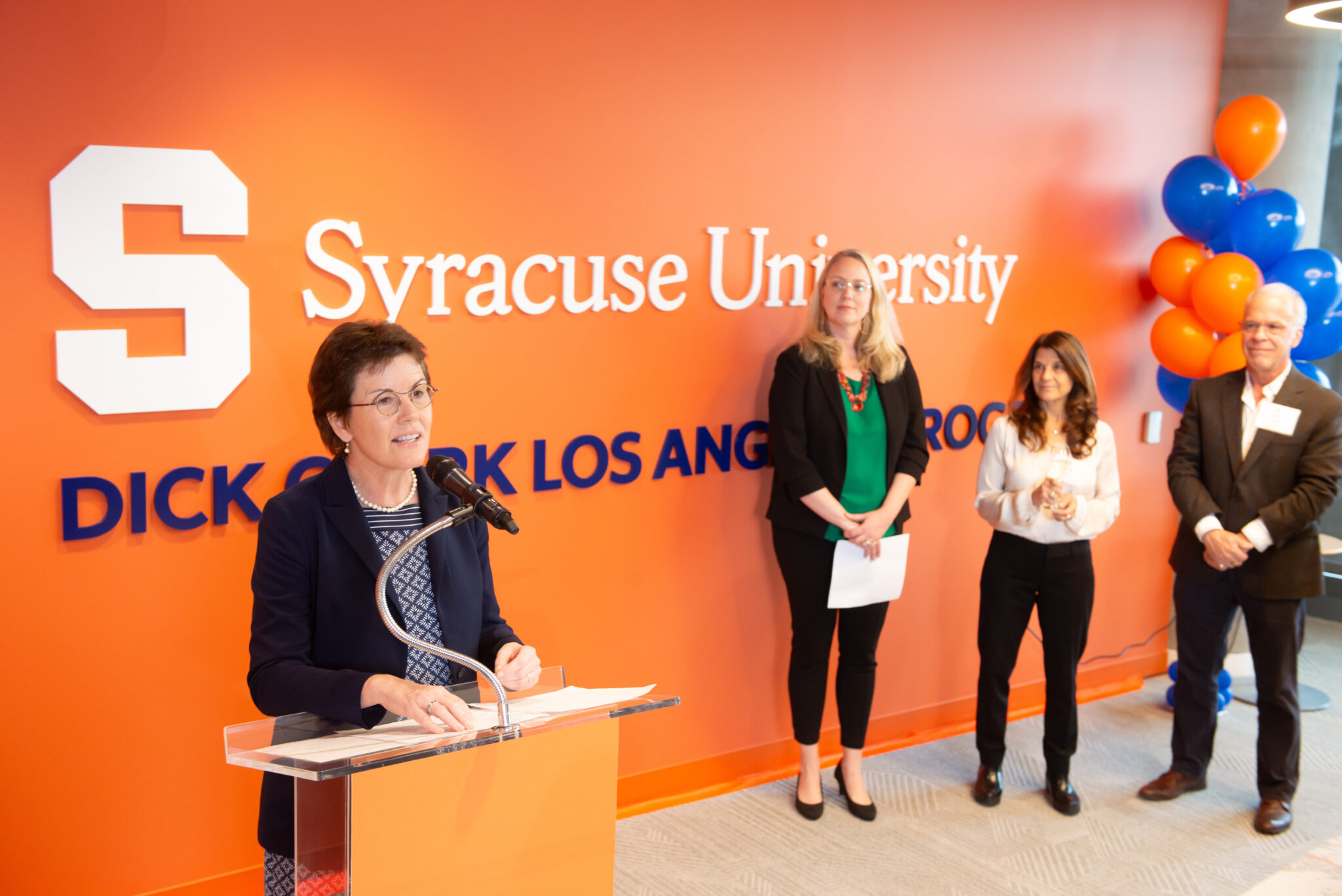 a person speaks at a podium while three other people look on