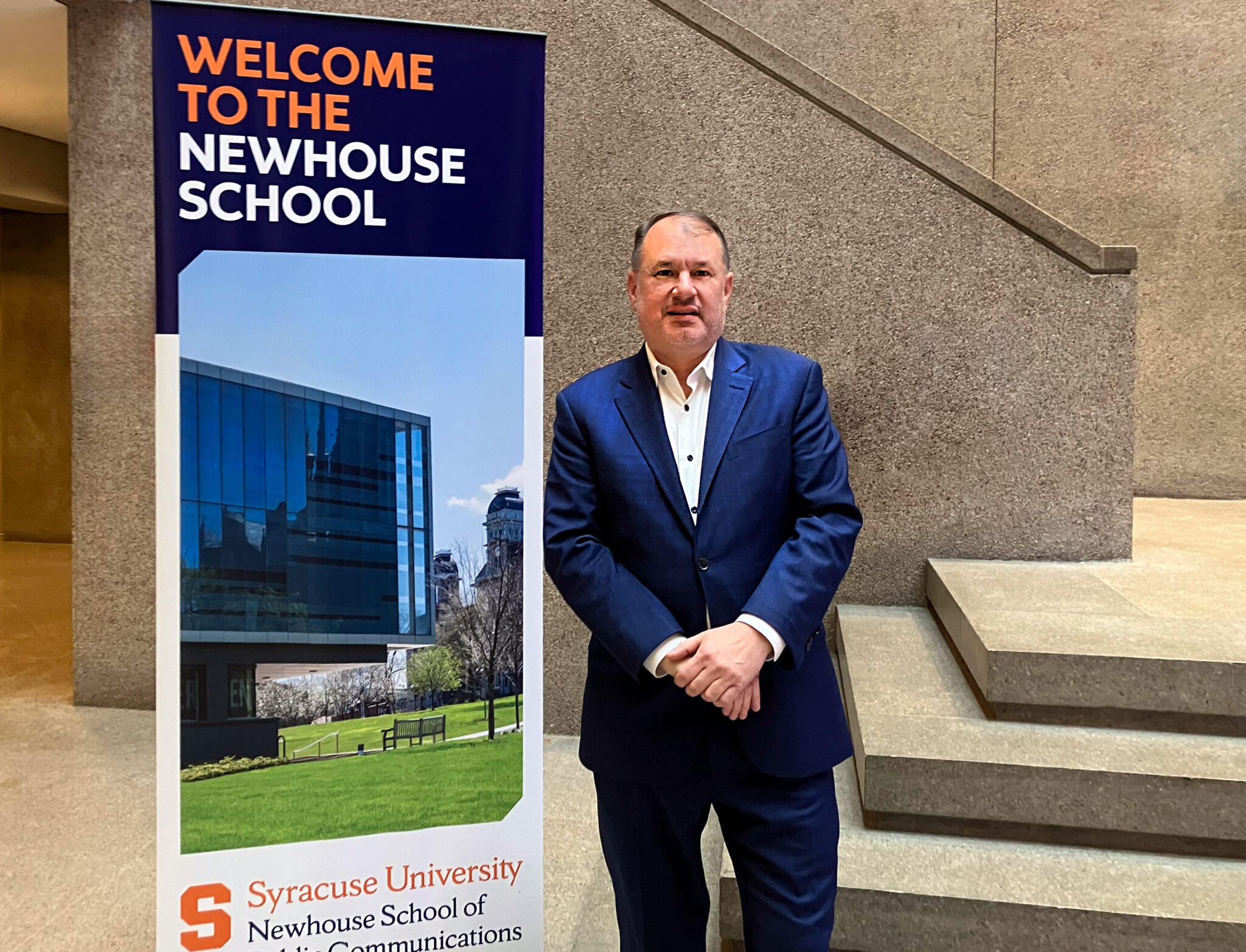 a person stands next to a sign that says "Welcome to the Newhouse School" in the Newhouse 1 lobby