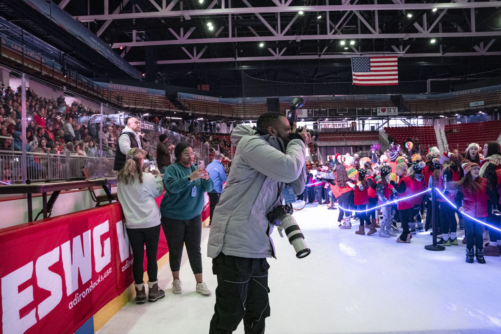 a photographer takes pictures of the opening ceremony of the empire state winter games in a hockey area full of people
