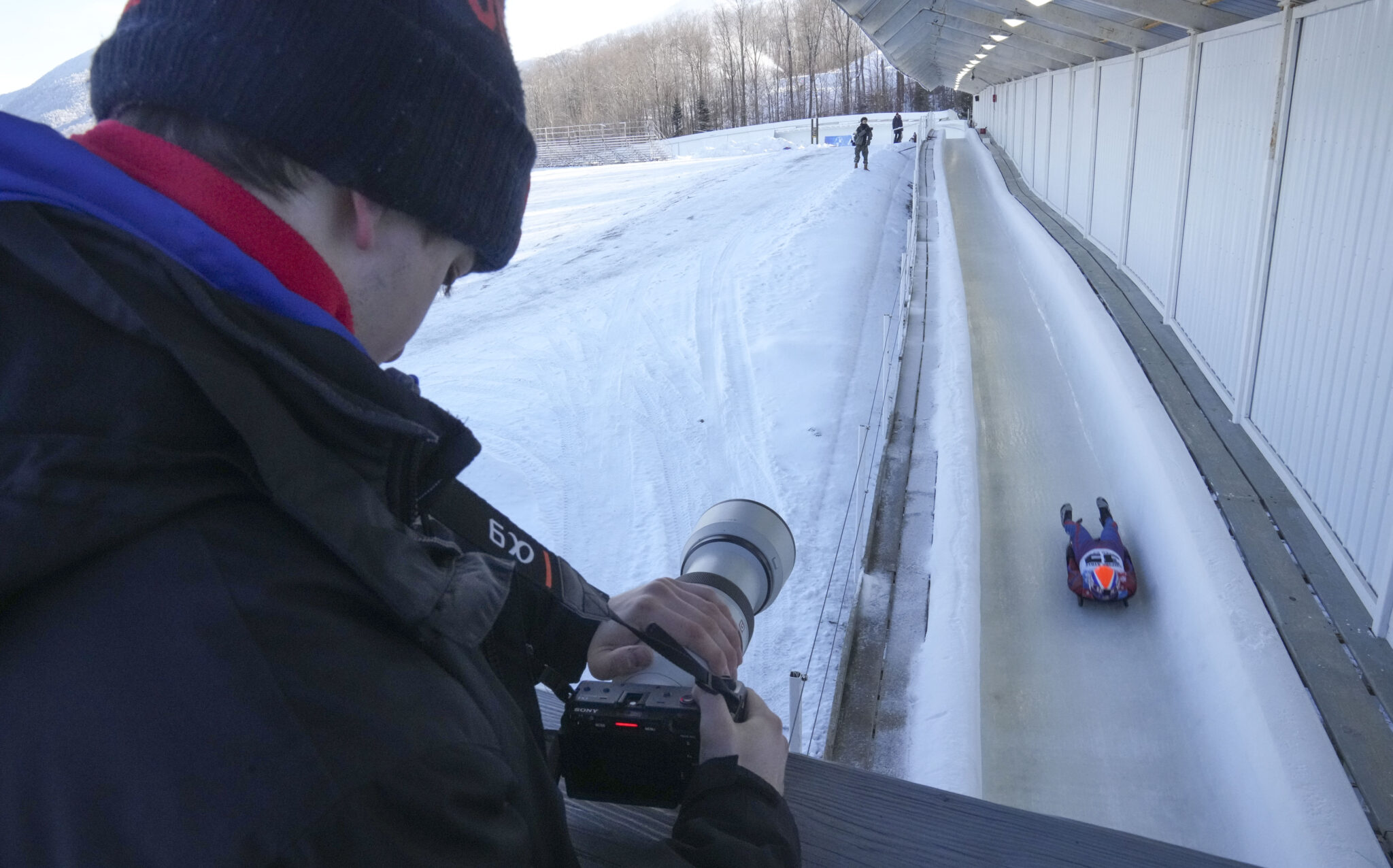 a photographer stands above a luge track and captures a an athlete going down the track