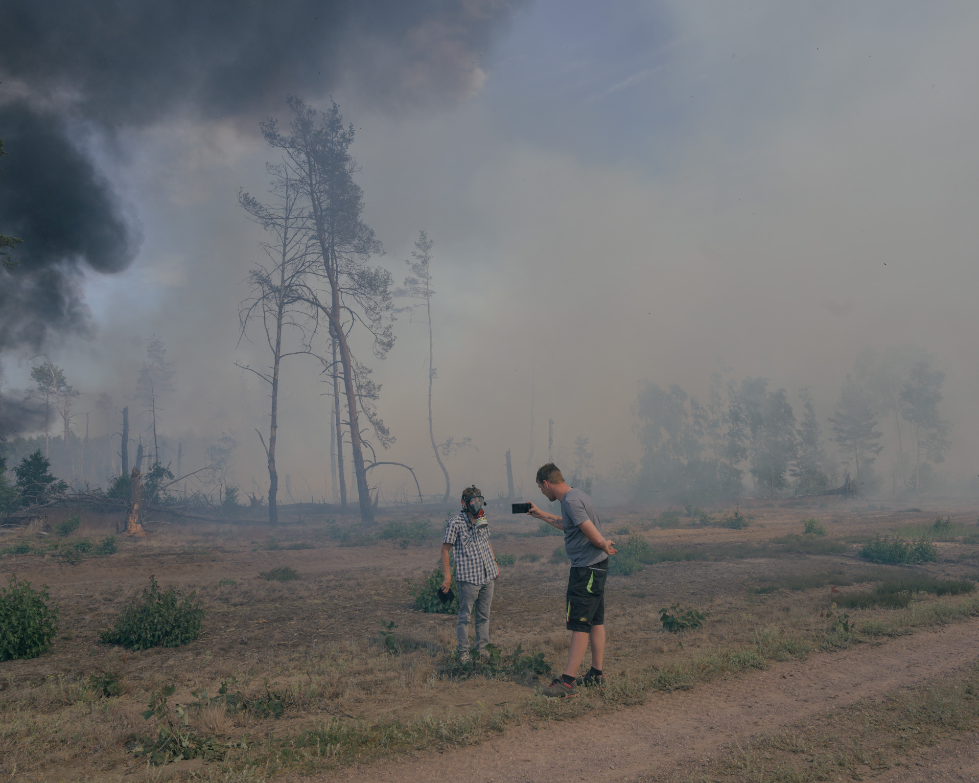 a person takes a photo of a person in a gas mask in front of a forest fire