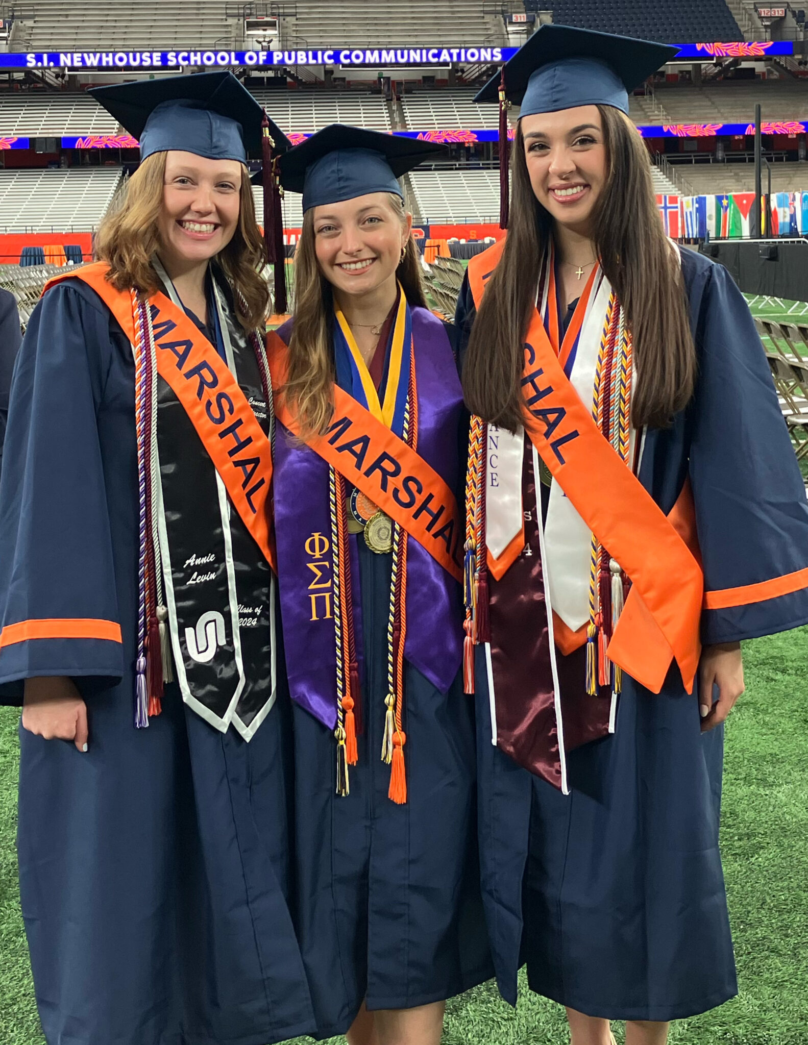 Three women dressed in graduation caps and gowns pose for a photo