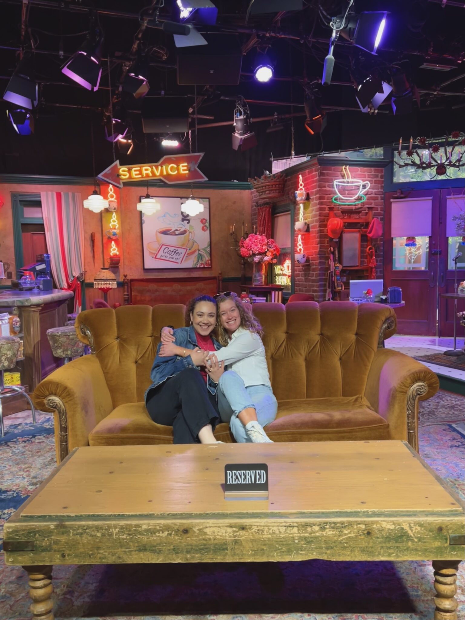 two people embrace each other while sitting on a couch on the set of the tv show "Friends"