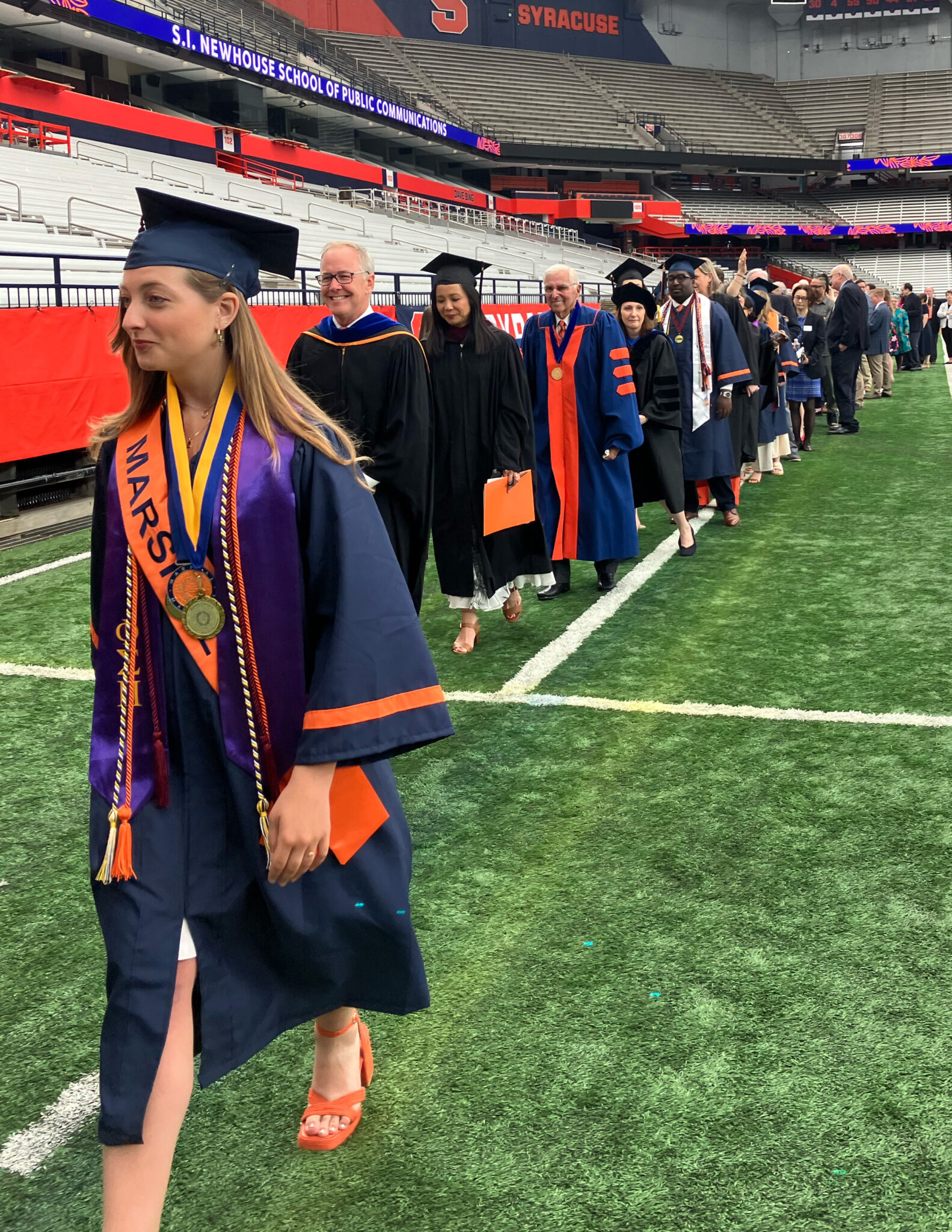 People in graduation caps and gowns walk to a stage before a ceremony