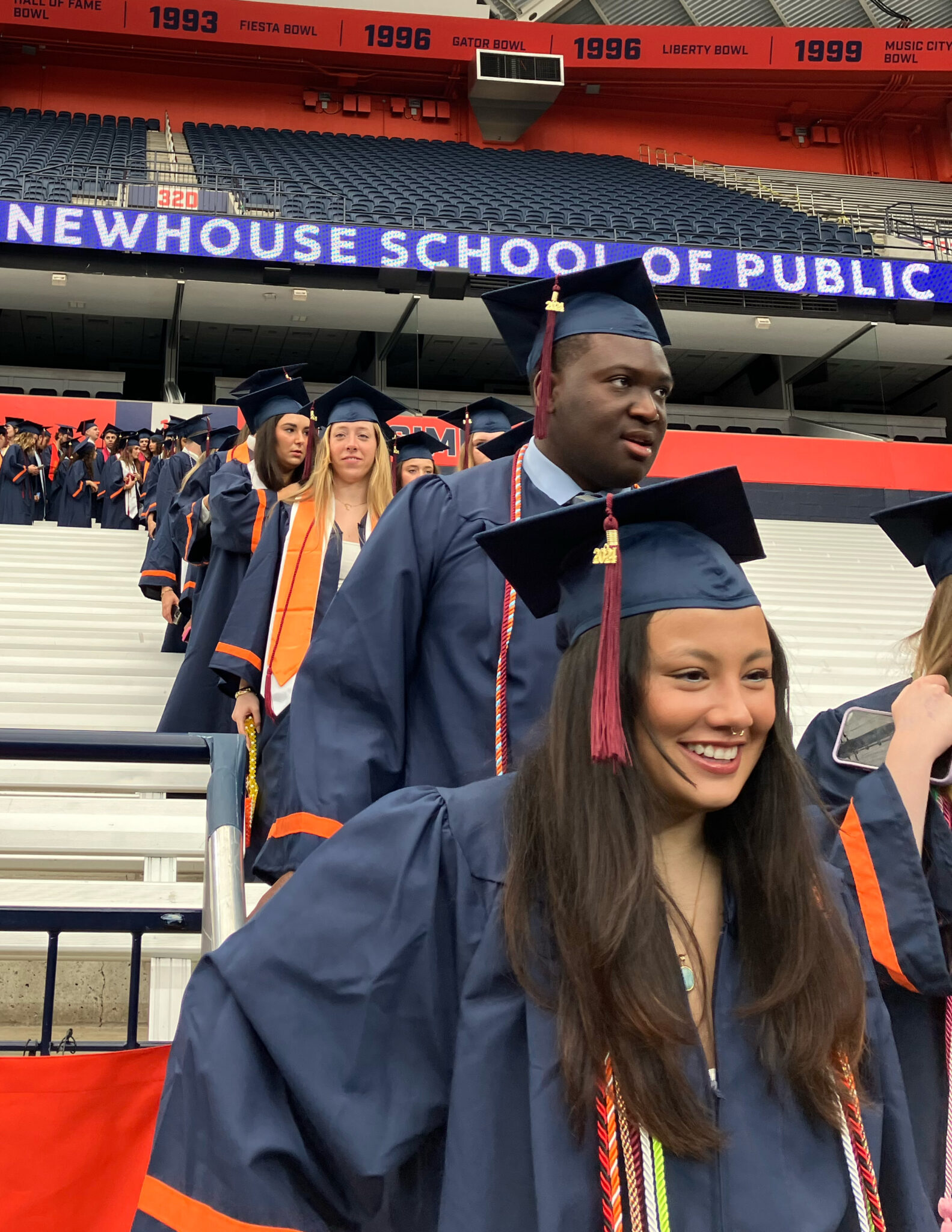 Students dressed in graduation caps and gowns walk down a flight of stairs