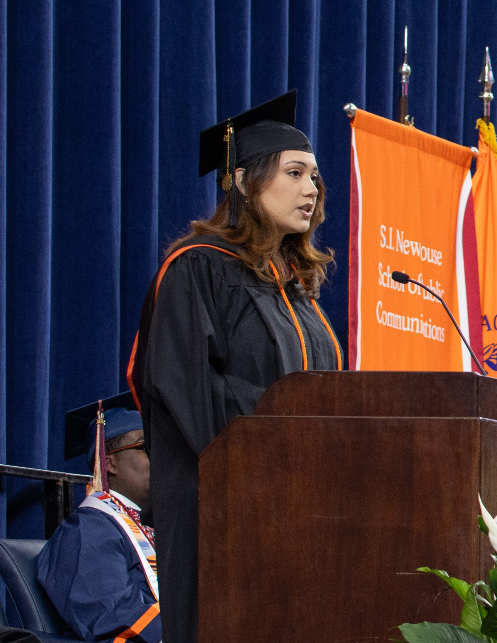 a person in a graduation cap and gown speaks at a podium