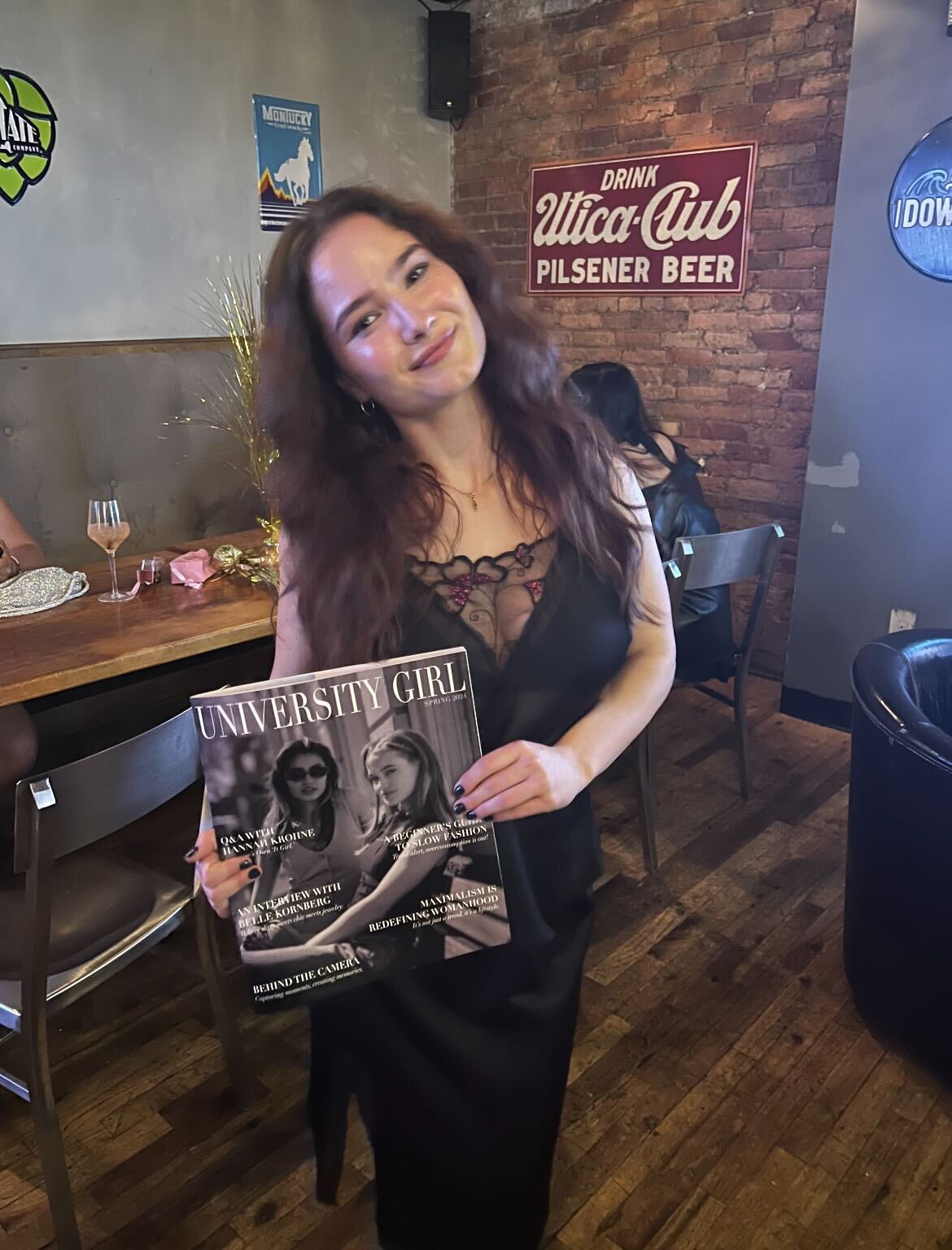 a person in a black dress stands holding a magazine
