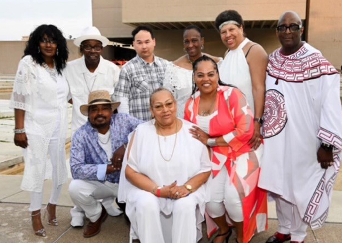 a group of people wear white clothing and smile and pose outside on a concrete patio