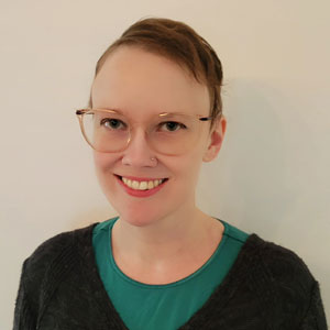 person with short brown hair and glasses poses for a headshot