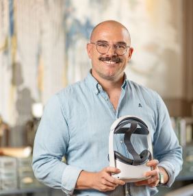 a person who is bald and has glasses and a mustache poses for a headshot in a light blue shirt