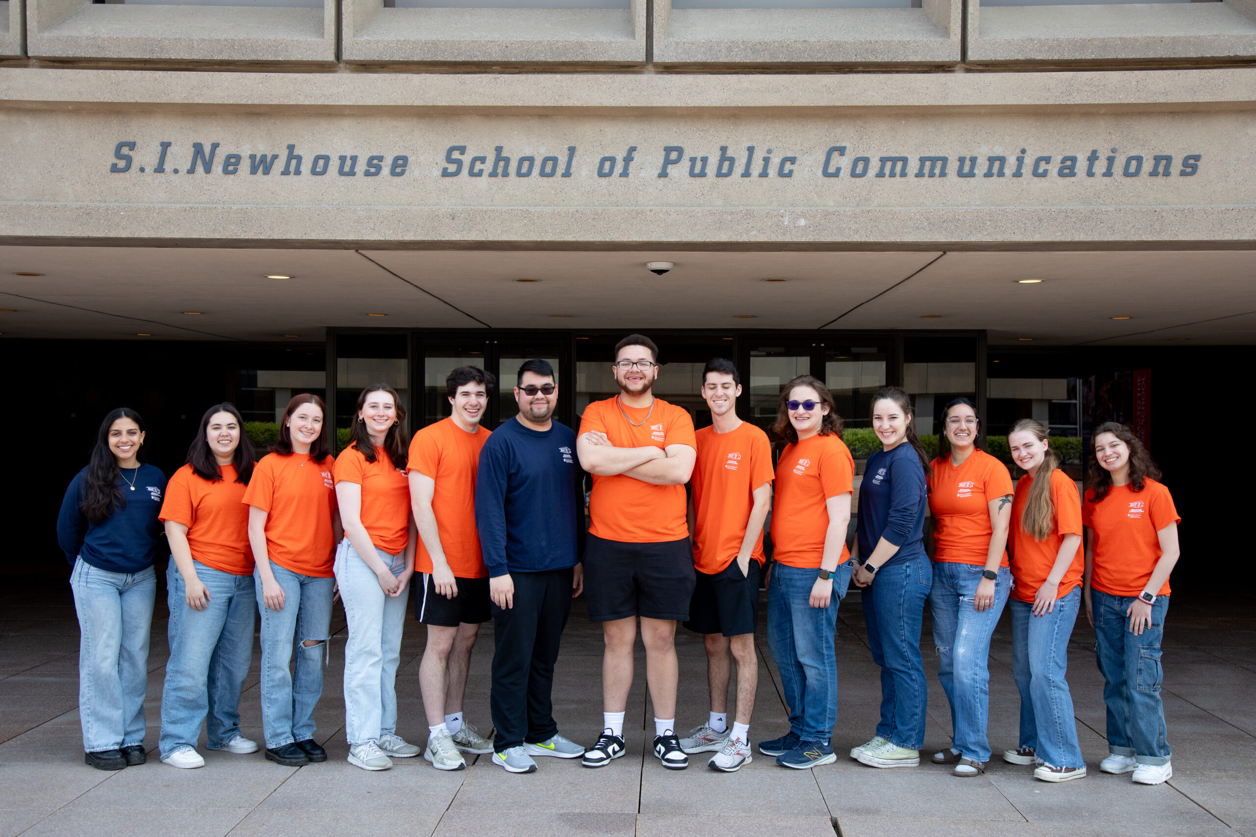 a group of people in orange and navy blue shirts stand outside on a patio and smile 