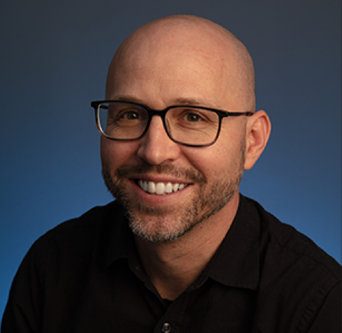 a person who is bald and has glasses and facial hair poses for a headshot in a black shirt
