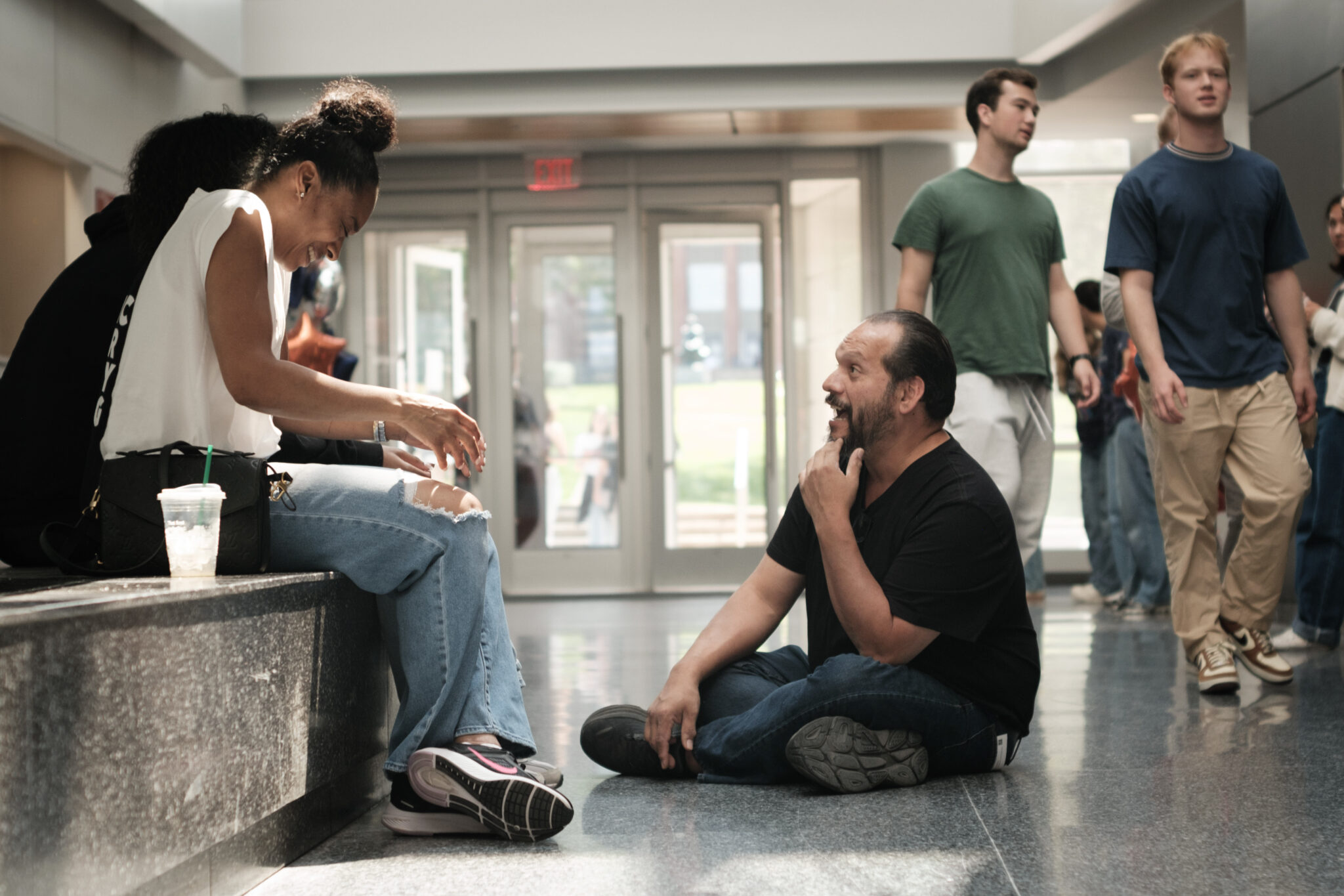 two seated people laugh while a person sitting on the floor in front of them talks