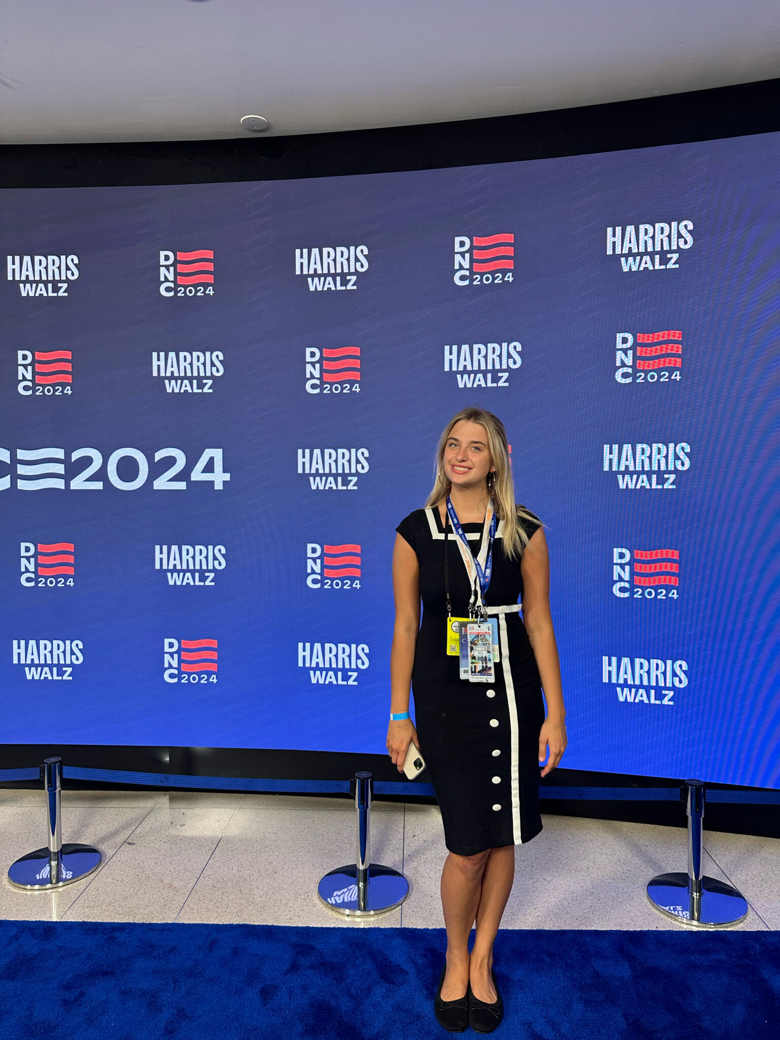 a person with blonde hair and wearing a black dress stands in front of a step and repeat at the Democratic National convention