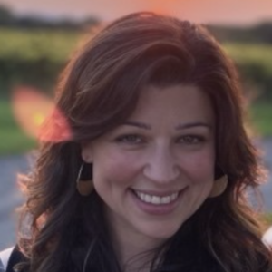 a person with brunette hair smiles for the camera while standing outside