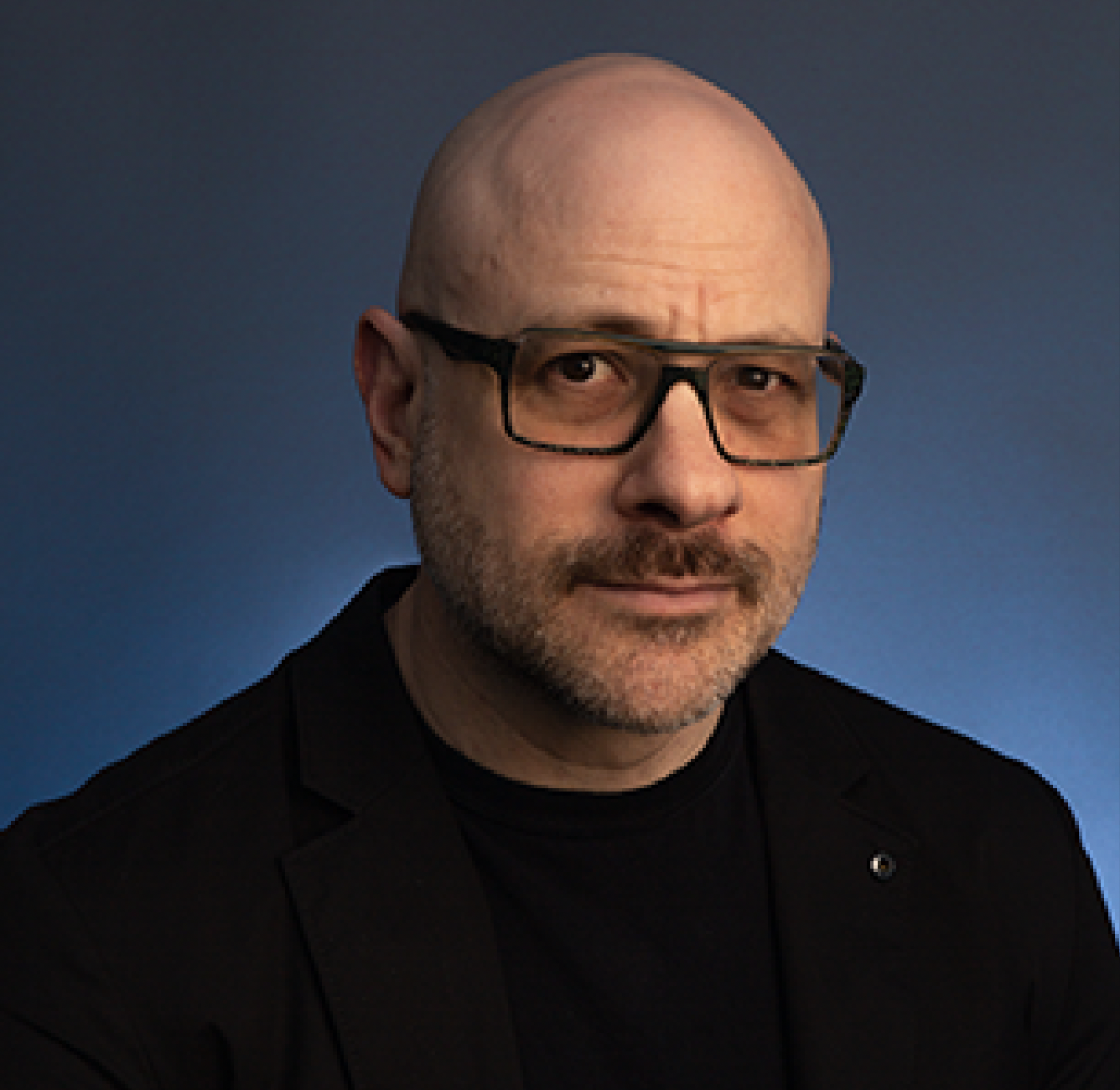 a person with glasses and a black shirt on poses for a headshot