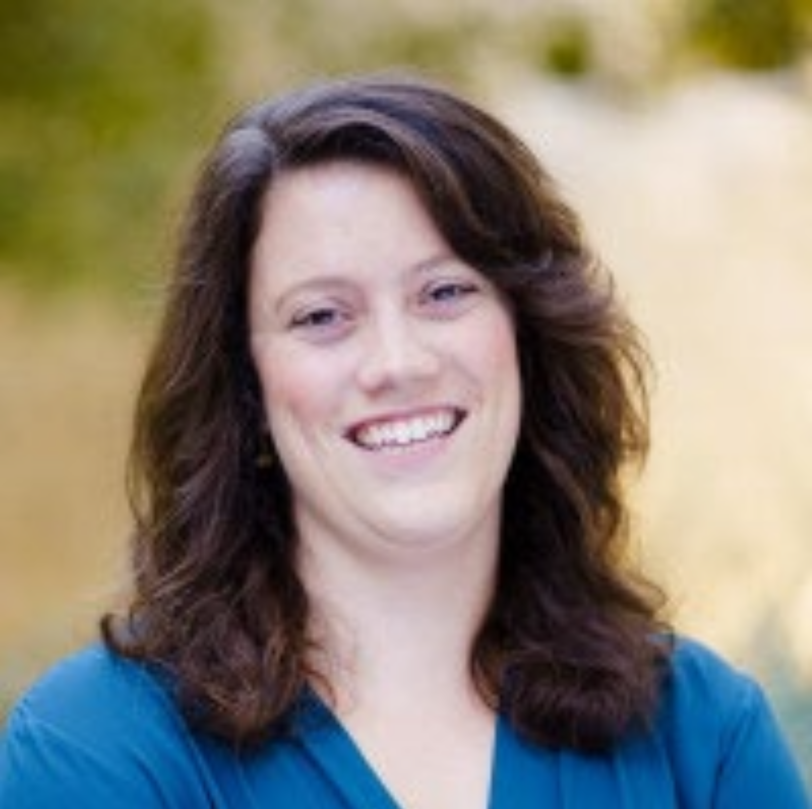 a person with long brown hair smiles for the camera in a professional headshot. they wear a blue shirt