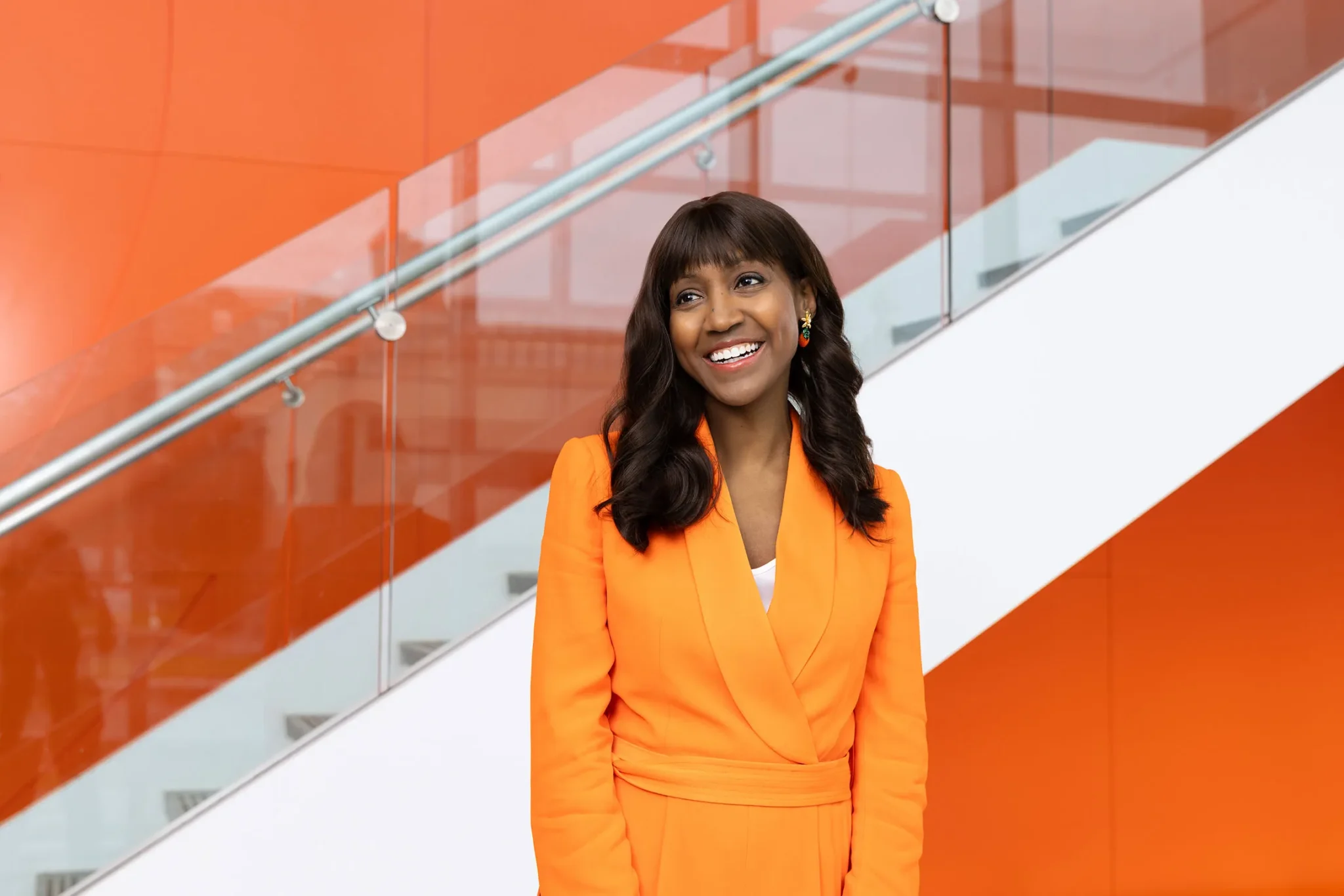 a person in an orange jacket poses at the bottom of a staircase