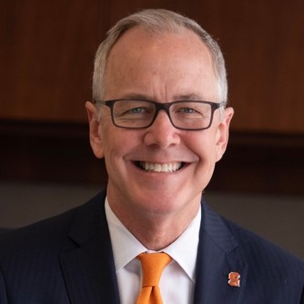 a person with glasses, blue suit jacket, white shirt and orange tie poses for a headshot