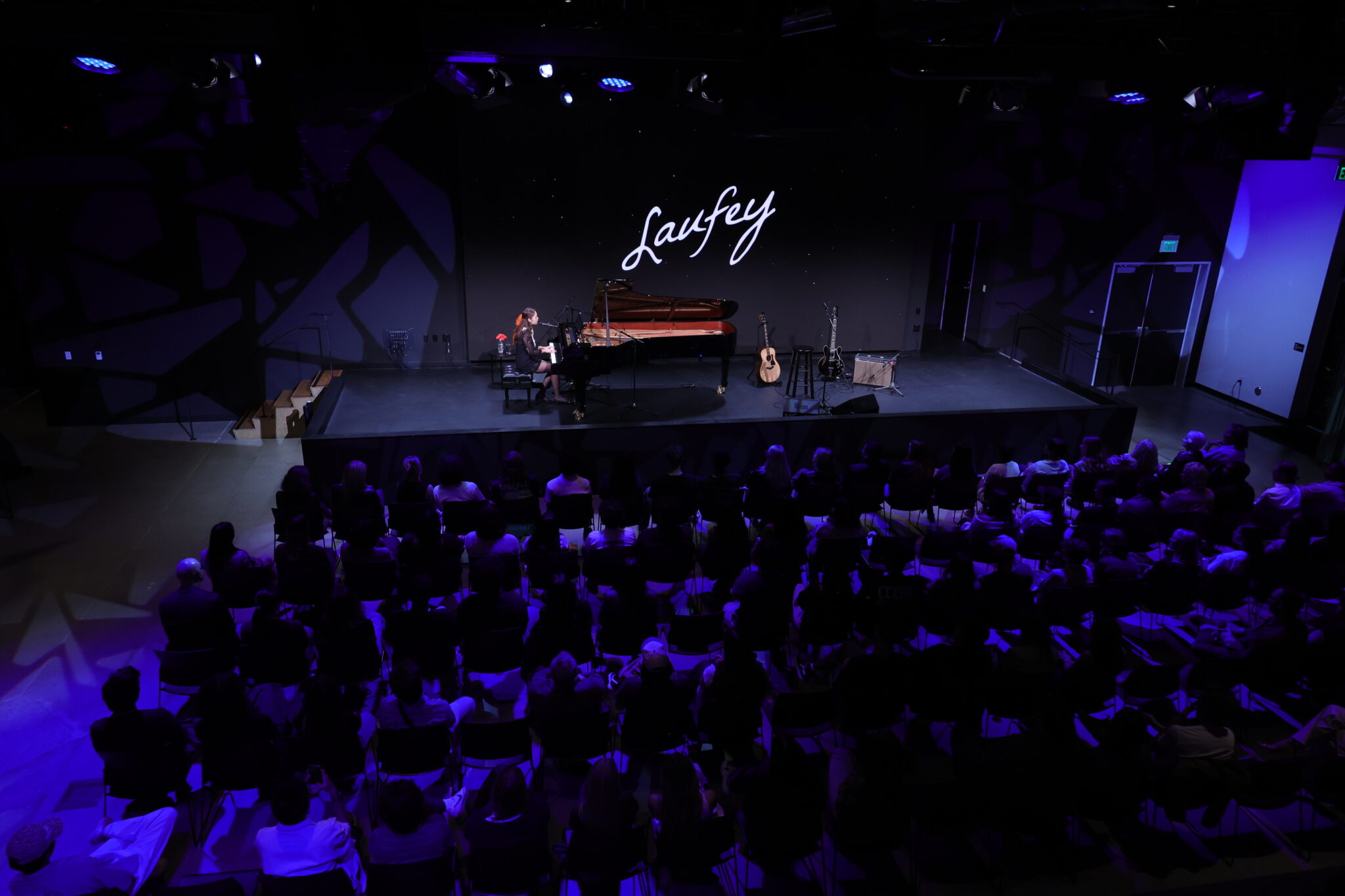 a person sits at a piano on a stage and performs while a large crowd watches