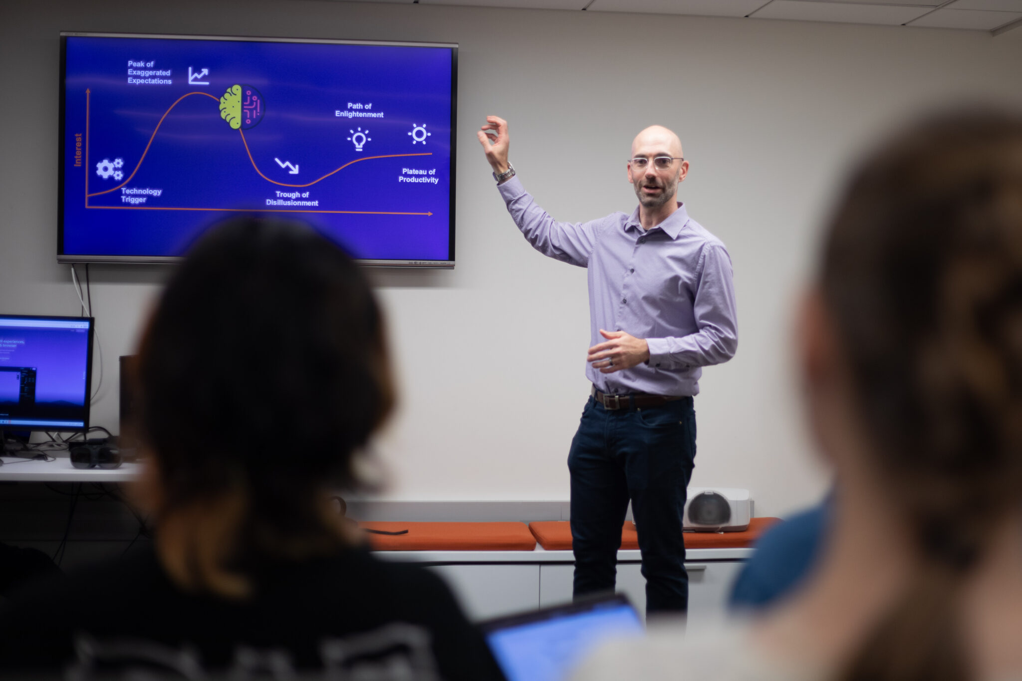 Advanced media management professor, Adam Peruta, gives a lecture to a class while pointing at a monitor.